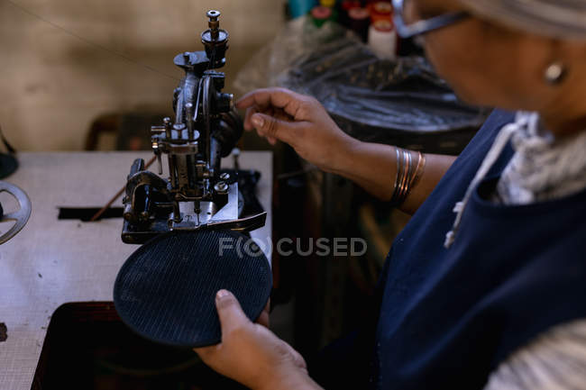 Elevated side view of a middle aged mixed race woman using a sewing machine at a hat factory — Stock Photo