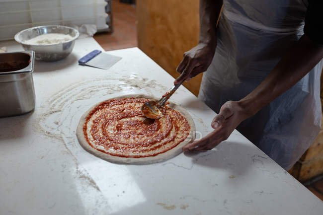 Side view mid section of male kitchen worker preparing a pizza base in a restaurant kitchen — Stock Photo
