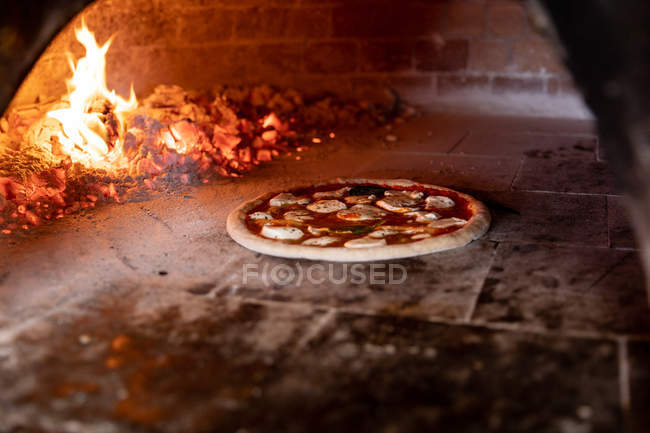 Vista frontal close-up de uma pizza assar em um forno de pizza, com as brasas quentes no fundo — Fotografia de Stock