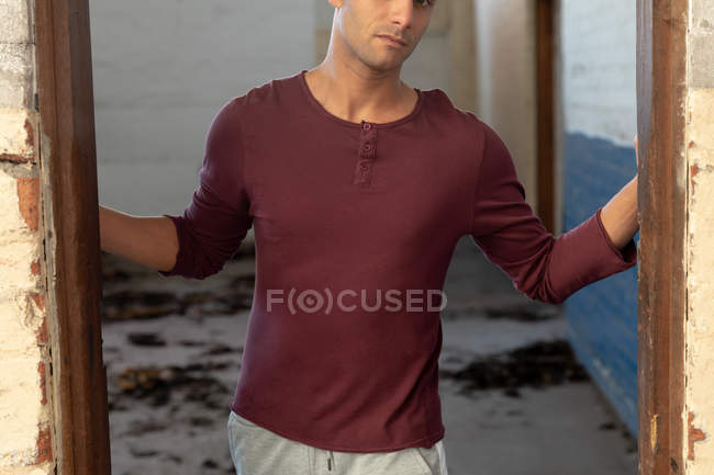 Frontansicht Mittelteil eines jungen Mannes, der in einer Tür steht und in eine verlassene Lagerhalle blickt — Stockfoto