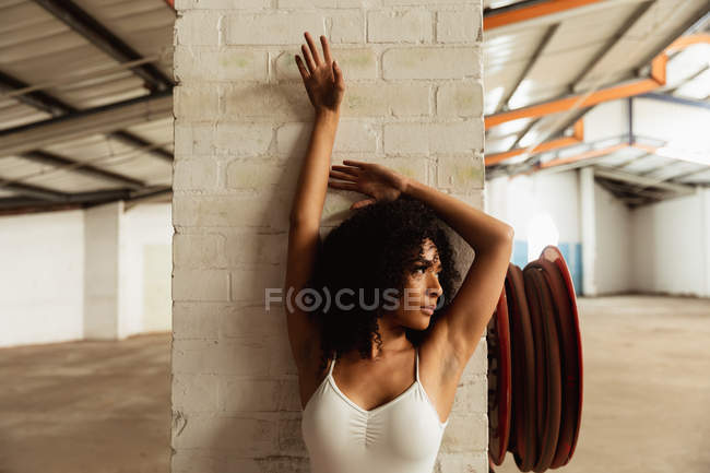 Front view close up of a young mixed race female ballet dancer dancing with arms raised and her back against a pillar and head turned to the side in an empty room at an abandoned warehouse — Stock Photo
