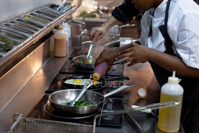 Side view mid section of an female chef and male chef working beside each other at a cooking station in a busy restaurant kitchen — Stock Photo