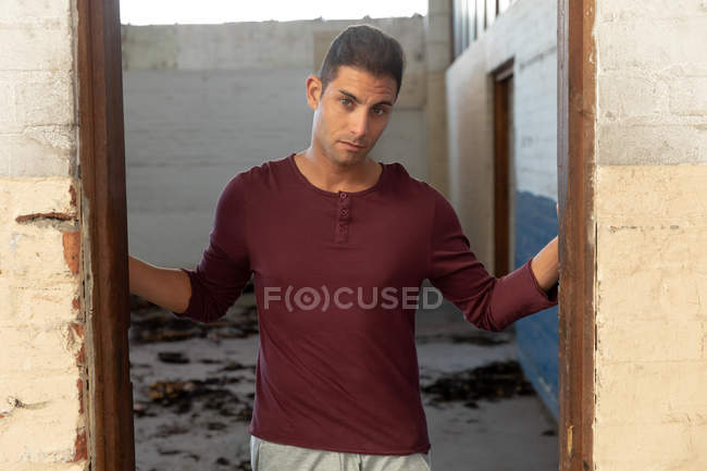 Портрет молодого чоловіка, що стоїть у дверному отворі, дивлячись на камеру на покинутому складі — стокове фото