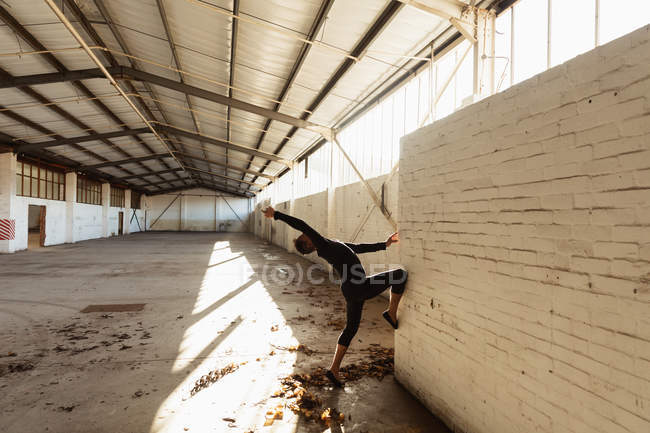 Side view of a young male ballet dancer wearing black dancing against a wall in an empty room at an abandoned warehouse — Stock Photo
