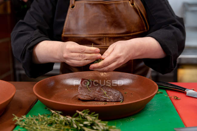 Вид спереду середня секція жіночого шеф-кухаря прикрашає м'ясо в страві на кухні ресторану — стокове фото