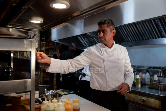 Vista lateral de cerca de un chef caucásico de mediana edad chequeando pedidos en la estación de pedidos en una cocina de restaurante - foto de stock