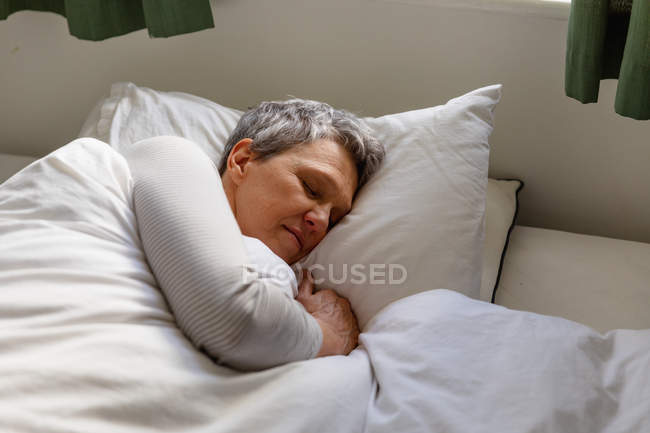 Vista lateral de cerca de una mujer caucásica madura con el pelo gris corto acostada en su lado en la cama en casa durmiendo - foto de stock