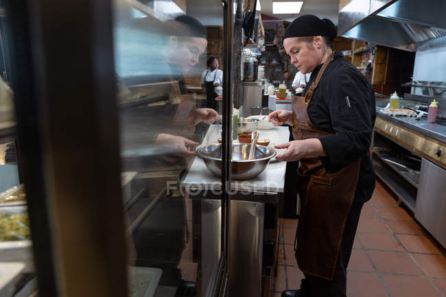 Side view close up of a young Caucasian female chef working at a counter in a busy restaurant kitchen, with — Stock Photo