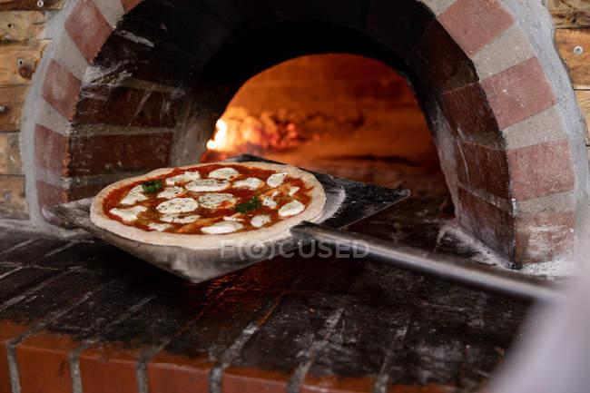 Nahaufnahme einer Pizza auf einer Schale, die zum Backen in einen Pizzaofen gelegt wird — Stockfoto