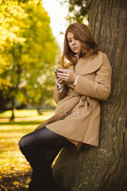 Hermosa mujer usando el teléfono móvil mientras está de pie en el parque . - foto de stock