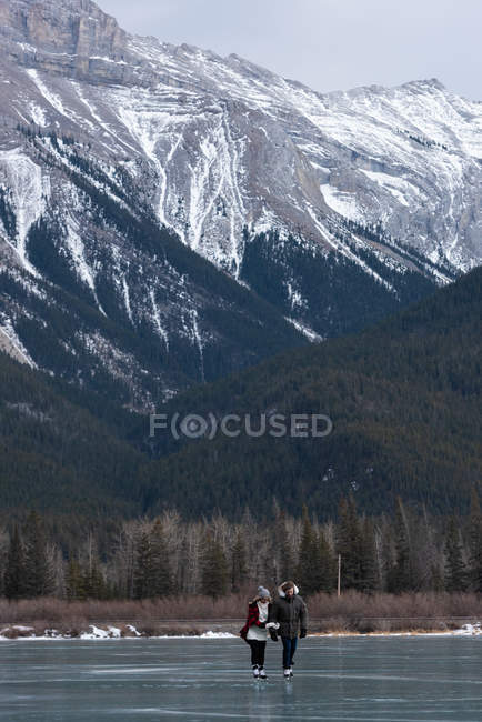 Vue de face du jeune couple romantique caucasien patinant ensemble dans un paysage enneigé naturel — Photo de stock
