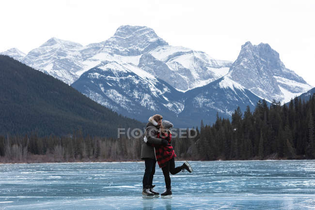 Vista lateral de la joven pareja caucásica besándose mientras están de pie en el paisaje nevado natural - foto de stock