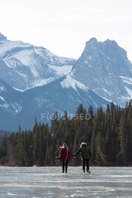 Rear view of young Caucasian couple skating together while holding hand in natural snowy landscape — Stock Photo