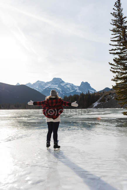 Rear view of happy Caucasian woman with arm stretched standing in natural snowy landscape in the background. — Stock Photo