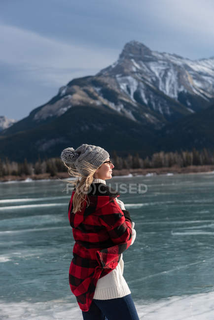 Side view of thoughtful young Caucasian blonde woman with winter outfit standing in natural snowy landscape in the background — Stock Photo