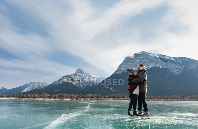 Vista lateral de um jovem casal romântico caucasiano abraçando uns aos outros em uma paisagem nevada natural no fundo . — Fotografia de Stock