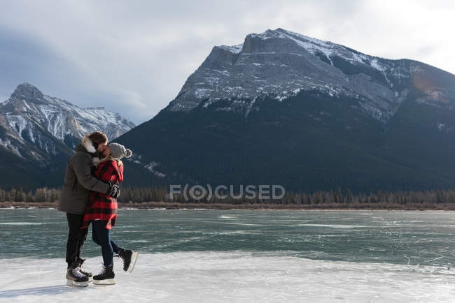 Вид збоку щаслива кавказька пара цілує один одного стоячи в природних сніжної краєвид у фоновому режимі — стокове фото