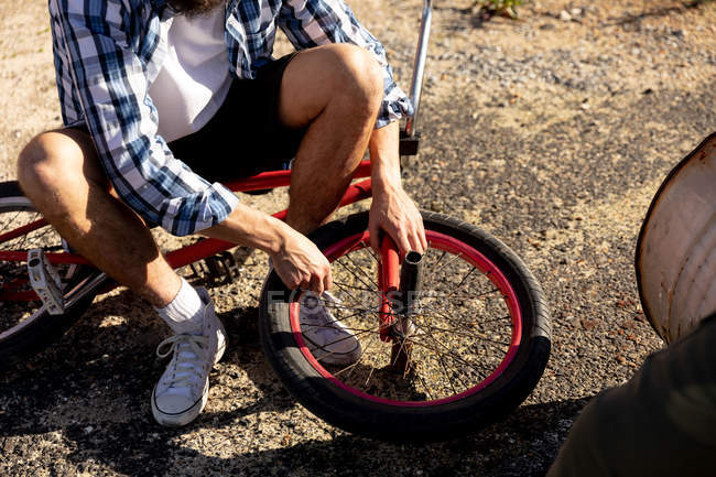 Вид спереду низька частина людини, що сидить на своєму велосипеді BMX і ремонтує колесо зовні на сонці — стокове фото