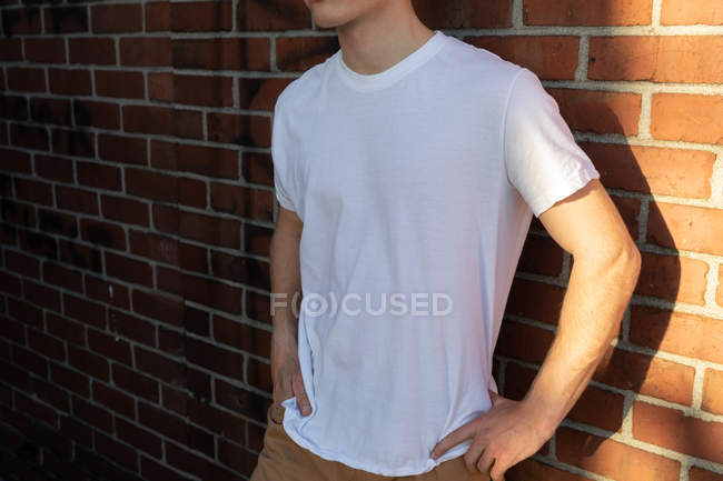 Seitenansicht Mittelteil eines jungen kaukasischen Mannes, der ein weißes T-Shirt trägt und mit den Händen an der Hüfte vor einer Backsteinmauer steht — Stockfoto