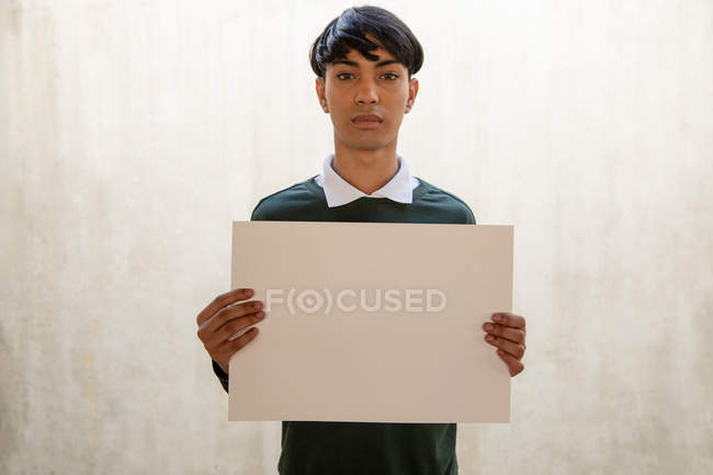 Портрет молодого трансгендера смешанной расы, держащего пустую табличку, напротив белой стены — стоковое фото