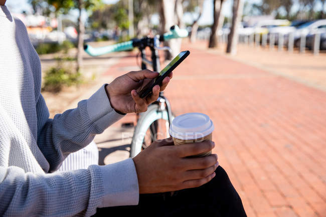 Vista lateral do homem usando um smartphone e segurando uma xícara de café na rua — Fotografia de Stock