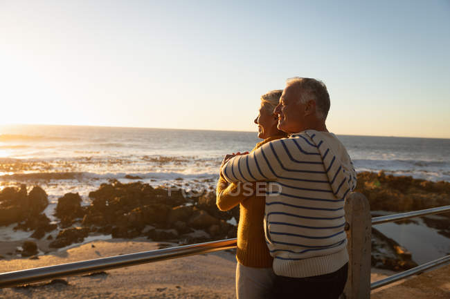 Vista lateral de perto de um homem e uma mulher caucasianos maduros abraçando o mar ao pôr-do-sol — Fotografia de Stock