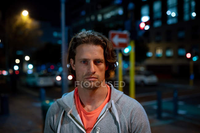 Porträt eines jungen kaukasischen Mannes auf der Straße, der während seines Workouts am späten Abend direkt in die Kamera blickt — Stockfoto