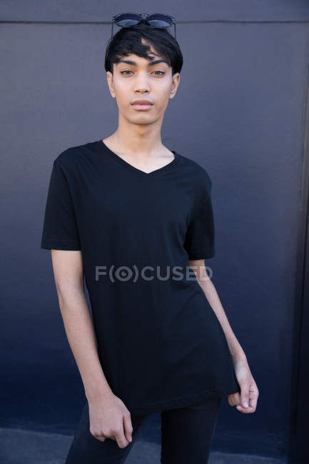 Retrato de un joven transgénero mestizo de moda en la calle contra una pared gris - foto de stock