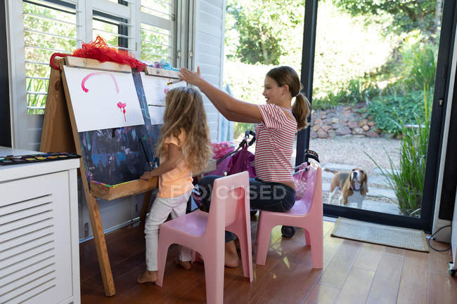 Vista laterale di una giovane ragazza caucasica e sua sorella che dipingono insieme a casa — Foto stock