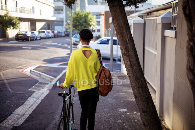 Vista trasera de un joven transexual de raza mixta de moda en la calle, caminando y sosteniendo una bicicleta - foto de stock