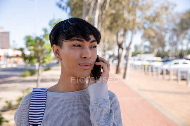 Vorderansicht eines modischen jungen Transgender-Erwachsenen mit gemischter Rasse auf der Straße, der auf dem Smartphone spricht — Stockfoto