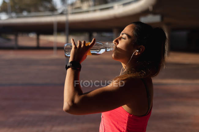 Seitenansicht einer jungen kaukasischen Frau in Sportkleidung, die während ihres Trainings an einem sonnigen Tag in einem Park Wasser trinkt — Stockfoto