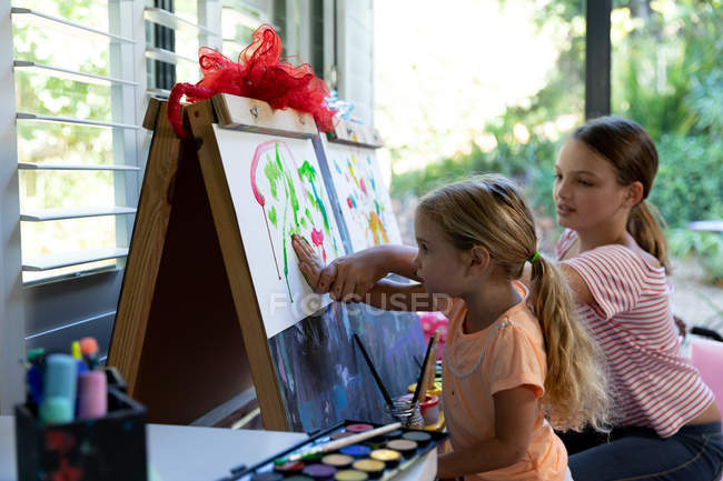 Side view of a young Caucasian girl and her tween sister painting together at home — Stock Photo