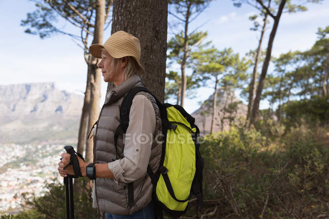 Бічний вид на зрілу кавказьку жінку, що тримає скандинавські пішоходи і милується краєвидом, з сільською місцевістю позаду неї. — стокове фото