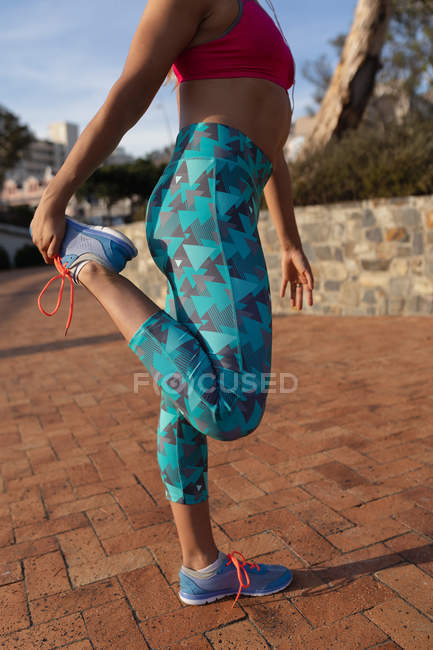 Visão lateral seção baixa de mulher vestindo roupas esportivas de pé segurando o pé e alongamento enquanto trabalhava em um dia ensolarado em um parque — Fotografia de Stock