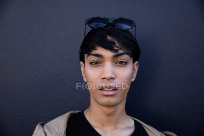 Retrato de un joven transgénero mestizo de moda en la calle contra una pared gris - foto de stock