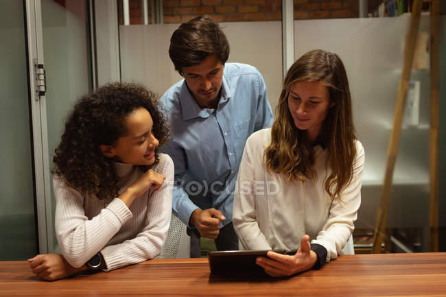 Передній план закриває вигляд молодої змішаної расової жінки і молодої кавказької жінки і чоловіка, які працюють в офісі творчого бізнесу, дивлячись разом на планшетний комп'ютер. — стокове фото