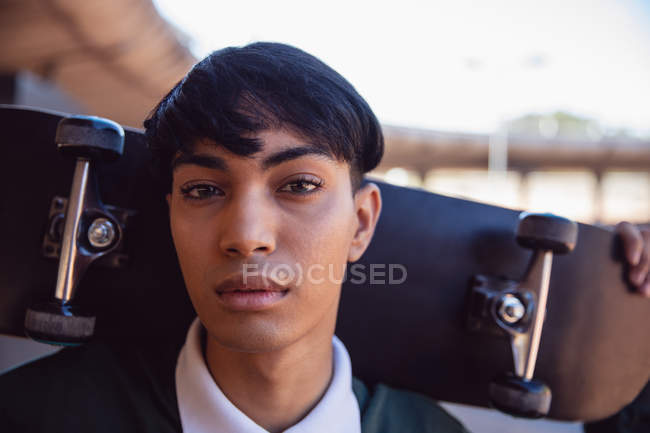 Retrato de un joven transgénero mestizo de moda en la calle, sosteniendo un monopatín - foto de stock