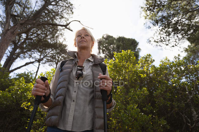 Vista frontale da vicino di una donna caucasica matura che regge bastoni da nordic walking e ammira la vista, con la campagna alle spalle — Foto stock