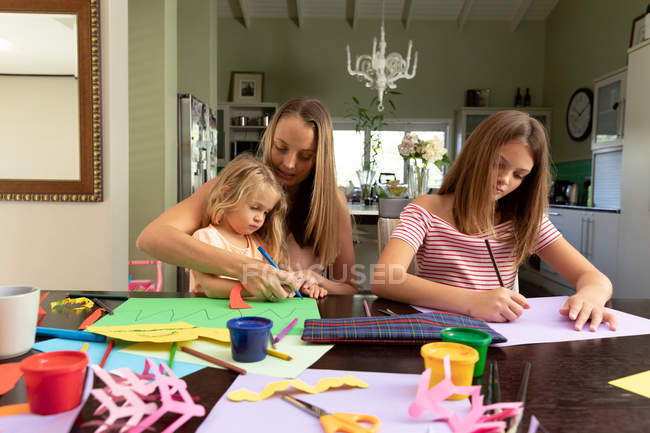 Vista frontal de uma jovem mulher caucasiana fazendo artesanato com suas filhas tween e mais jovens em sua sala de estar — Fotografia de Stock
