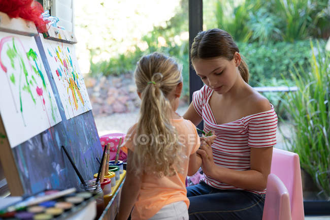 Vista frontal de uma jovem caucasiana e sua irmã tween pintura juntos em casa — Fotografia de Stock