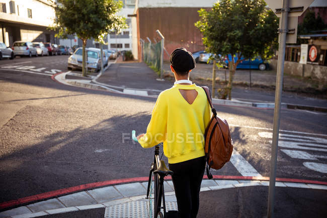 Raer vista de um jovem elegante mestiço transexual adulto na rua, de pé e segurando uma bicicleta — Fotografia de Stock