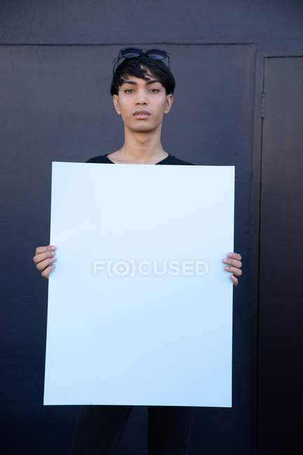 Retrato de una joven transexual mestiza sosteniendo un letrero en blanco, mirando a la cámara - foto de stock