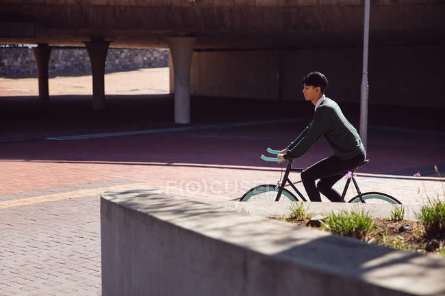 Vista lateral de un joven transgénero mestizo de moda en la calle, en bicicleta - foto de stock