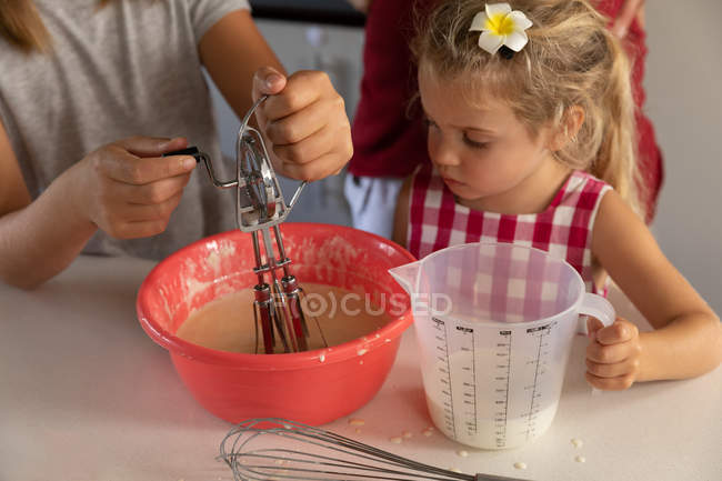 Frontansicht eines jungen kaukasischen Mädchens und ihrer Zwillingsschwester beim Mischen von Lebensmitteln in einer Schüssel, die zusammen in der Küche kocht — Stockfoto