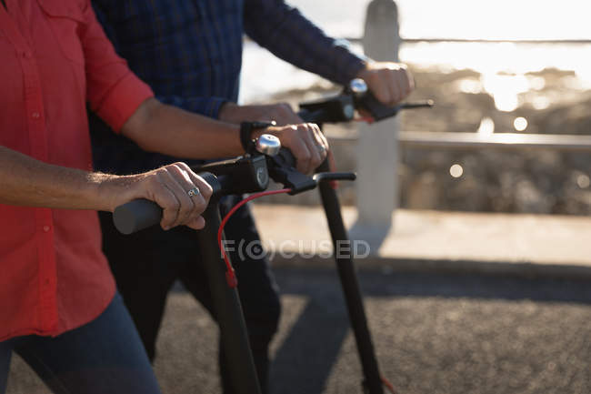 Side view mid section of man and woman riding e scooters by the sea at sunset — Stock Photo