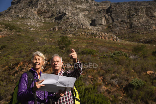 Front view close up of a mature Caucasian man and woman reading a map and pointing during a walk in a rural setting, with mountains in the background — Stock Photo