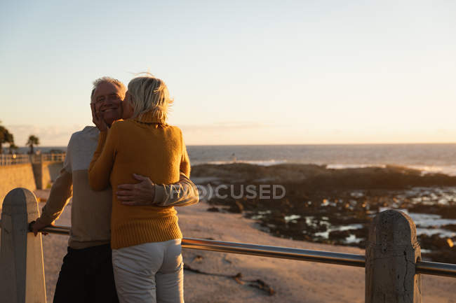 Rear view close up of a mature Caucasian man and woman embracing and kissing by the sea at sunset — Stock Photo