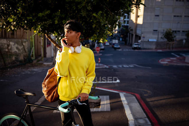 Vista frontal de un joven transexual de raza mixta de moda en la calle, de pie y sosteniendo una bicicleta - foto de stock