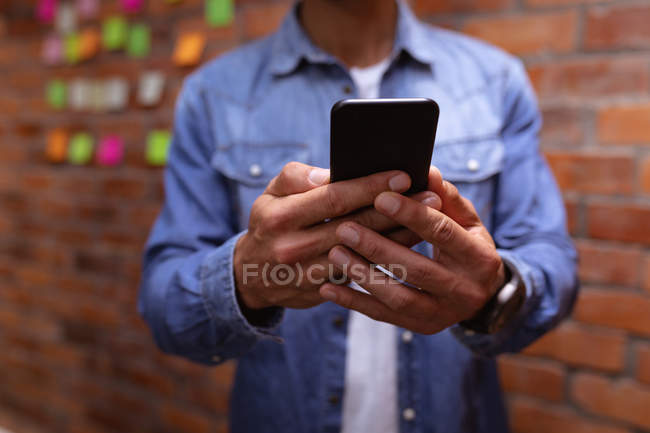 Front view mid section of man using a smartphone standing in the office of a creative business — Stock Photo